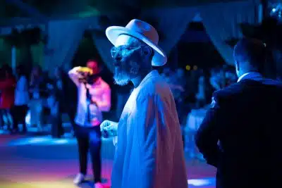 a man in a white hat and sunglasses standing in front of a group of people