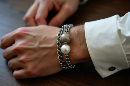Bracelet perle et bracelet acier portés ensemble au poignet d'un homme sur un fond en bois sombre
