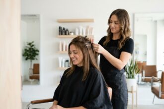 Pose d'extensions de cheveux en salon par une coiffeuse professionnelle sur une cliente aux cheveux bruns naturels mi-longs